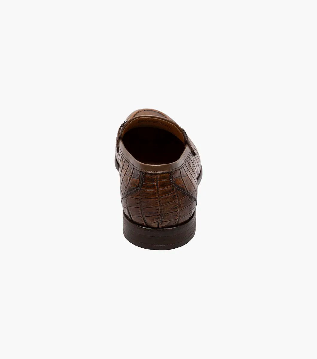 The STACY ADAMS Ferdinand Moc Toe Bit Slip On in Cognac features croco print leather, a decorative metal bit, and a cushioned memory foam footbed, displayed on a white background.