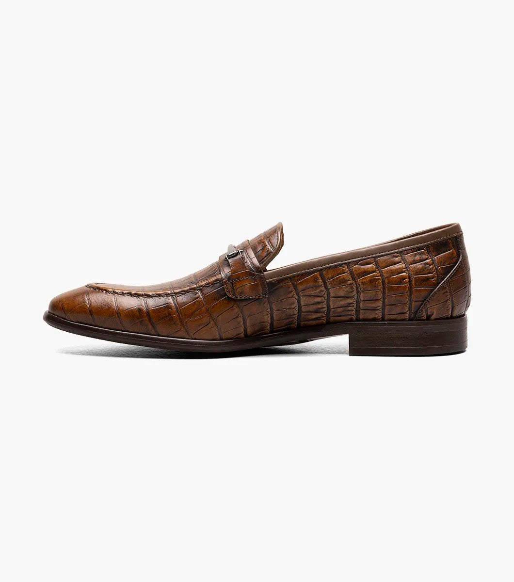 The STACY ADAMS Ferdinand Moc Toe Bit Slip On in Cognac features croco print leather, a decorative metal bit, and a cushioned memory foam footbed, displayed on a white background.